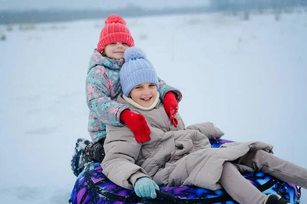 İki çocuk, serin bir parkta sıcak şapkalar ve eldivenlerle karlı bir tepeden aşağı kayarak gülüyor ve birlikte eğleniyorlardı..