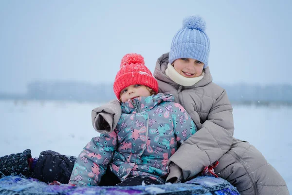 Soğuk bir günde, hafif kar yağışı olan neşeli bir anın tadını çıkarırlarken, iki çocuk karda kızağın üzerinde, kalın kışlık giysiler giyerek birlikte oturuyorlar..