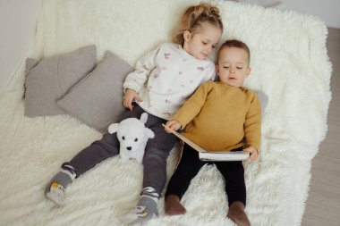 İki çocuk yumuşak bir kanepede. Bir çocuk bir kitap tutuyor ve diğeri bir oyuncakla oynuyor. Parlak bir salonda birlikte vakit geçiriyorlar..