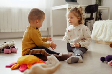 İki çocuk yerde oturup renkli oyuncaklarla çevrili boş bir kağıt parçasıyla oynuyorlar. Gülücüklerini paylaşıyorlar ve oyun saatleriyle meşgul oluyorlar..