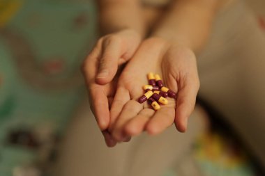 Bir insanın elleri, akşam yumuşak bir yüzey üzerinde kapalı otururken renkli kapsüller gösterir. Ayarlar evde rahat bir an olduğunu gösteriyor..