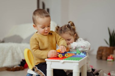 İki genç çocuk, iyi aydınlatılmış bir odadaki küçük bir masada yapı taşlarıyla yaratıyorlar. Oyun oynarken tasarımlarına odaklanır ve fikirlerini paylaşırlar..