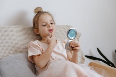 Genç bir kız kanepede oturur, makyaj yaparken aynaya bakar. İyi aydınlatılmış bir odada eğleniyor..