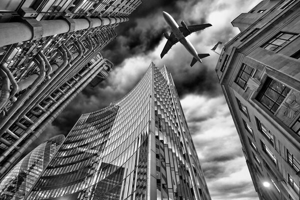 A jet plane flying low over Three different kind of architecture with commercial office buildings exterior. Evening view at bottom skyscrapers.Black and white