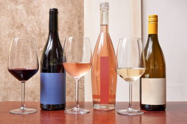 Üç farklı şarap şişesi ve üç bardak dokulu arka planda.