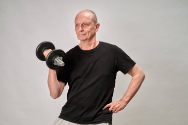 65 yaşında spor giyimli bir adam. Biraz da halterli egzersiz yapıyor.