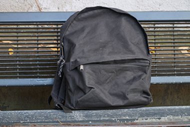 Açık havada, metal bankta kullanılmış siyah sırt çantası.
