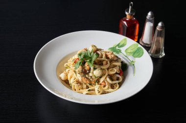 Siyah ahşap bir masa üzerinde deniz mahsulleri ile bir tabak tagliatelle makarna.