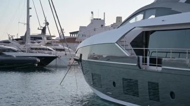 Limasol, Kıbrıs - 22 Mayıs 2025: Limasol Marina. Yat limanına yanaşmış büyük, parlak, beyaz bir yatın yakın plan görüntüsü. Arka planda yakınlarda demirlemiş başka yatlar ve tekneler var..