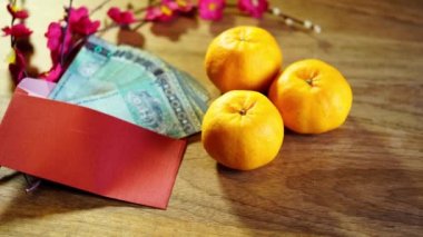 Mandalina portakalları ve ahşap zemin üzerinde para olan Çin kırmızı zarfı.