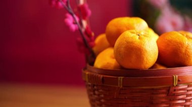 Bir sepet mandalina ve Çin Yeni Yıl Festivali süslemeleri, kırmızı paket, erik çiçeği, Ingot ve kırmızı arka planda fener..