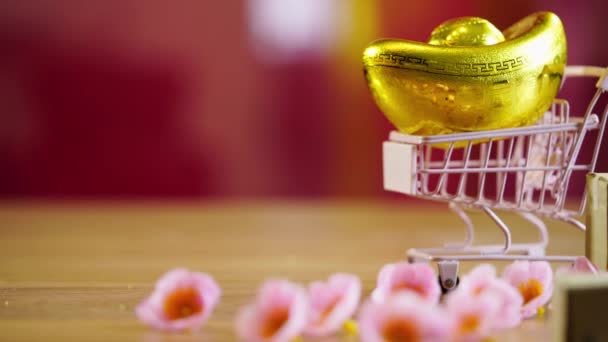 Einkaufswagen Mit Chinesischen Goldbarren Ornamenten Auf Der Hölzernen Tischplatte — Stockvideo