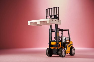 Pembe arka planda ahşap paletli oyuncak forklift.