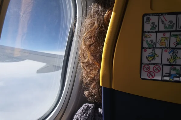 Flying female passenger looking through the window of the airplane — Stock Photo, Image