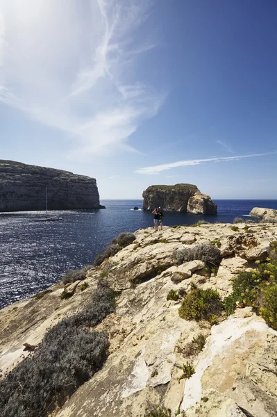 Malta Island, Gozo, tourists look at a sailing boat in the Dweira Lagoon and the rocky coastline near the Azure Window Rock — Stock Photo, Image