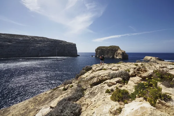 Insula Malta, Gozo, turiștii se uită la o barcă cu vele în laguna Dweira și la coasta stâncoasă din apropierea stâncii Azure Window Rock — Fotografie, imagine de stoc