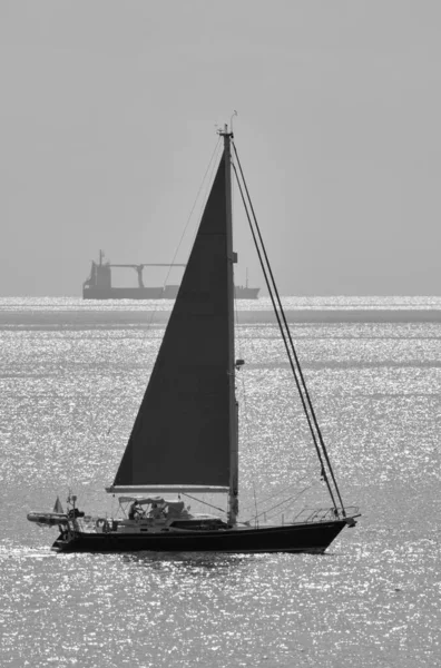 İtalya, Sicilya, Akdeniz Sicilya Kanalı 'nda yelken açan bir tekne ve arka planda bir kargo gemisi.
