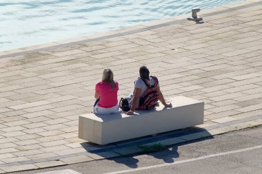 İtalya, Sicilya, Marina di Ragusa (Ragusa Eyaleti); limandaki bankta oturan çift 