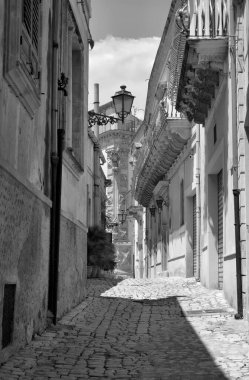 Arka planda İtalya, Sicilya, Scicli (Ragusa ili), eski barok binalar ve Barok Beneventano Sarayı cephesi yer almaktadır.
