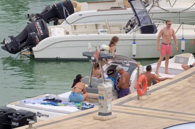 İtalya, Sicilya, Akdeniz, Marina di Ragusa (Ragusa ili); 26 Haziran 2021, büyük bir kauçuk bot ve limandaki lüks yatlarda yaşayan insanlar - EDITORIAL