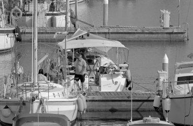 İtalya, Sicilya, Akdeniz, Marina di Ragusa (Ragusa Eyaleti); 1 Temmuz 2021, limandaki bir yelkenli ve lüks yatlarda yaşayan insanlar - EDITORIAL