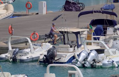 İtalya, Sicilya, Akdeniz, Marina di Ragusa (Ragusa Eyaleti); 9 Temmuz 2021, limanda bisiklet, motorlu tekne ve lüks yatlarda yaşayan kadın - EDITORIAL