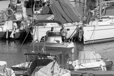 İtalya, Sicilya, Akdeniz, Marina di Ragusa (Ragusa Eyaleti); 10 Temmuz 2021, limanda bir motorlu tekne ve lüks yatlarda erkekler - EDITORIAL