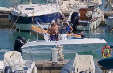 İtalya, Sicilya, Akdeniz, Marina di Ragusa (Ragusa Eyaleti); 10 Temmuz 2021, limanda bir motorlu tekne ve lüks yatlarda erkekler - EDITORIAL
