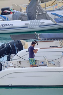 İtalya, Sicilya, Akdeniz, Marina di Ragusa (Ragusa Eyaleti); 19 Temmuz 2021, limandaki bir motorlu teknede adam - EDITORIAL