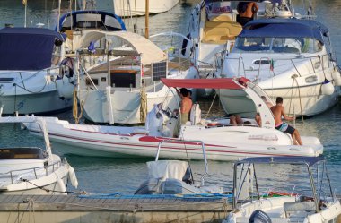 İtalya, Sicilya, Akdeniz, Marina di Ragusa (Ragusa ili); 14 Ağustos 2021, limandaki kauçuk bir tekne ve lüks yatlarda yaşayan insanlar - EDITORIAL