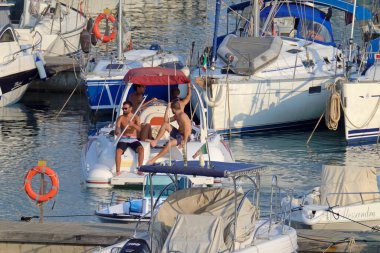 İtalya, Sicilya, Akdeniz, Marina di Ragusa (Ragusa ili); 14 Ağustos 2021, limandaki kauçuk bir tekne ve lüks yatlarda yaşayan insanlar - EDITORIAL