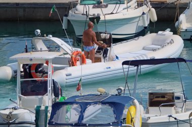 İtalya, Sicilya, Akdeniz, Marina di Ragusa (Ragusa Eyaleti); 22 Ağustos 2021, limandaki kauçuk bir tekne ve lüks yatlarda adam - EDITORIAL