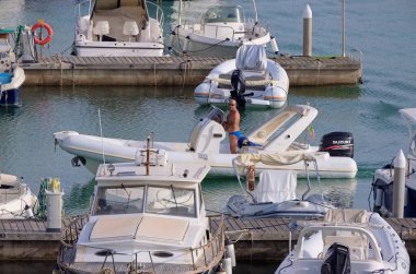 İtalya, Sicilya, Akdeniz, Marina di Ragusa (Ragusa Eyaleti); 17 Eylül 2021, limandaki kauçuk bir tekne ve lüks yatlarda adam - EDITORIAL