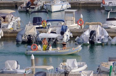 İtalya, Sicilya, Akdeniz, Marina di Ragusa (Ragusa Eyaleti); 17 Eylül 2021, limanda kauçuk bir tekne ve lüks yatlarda bir çift - EDITORIAL