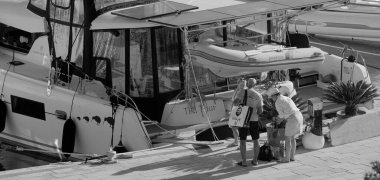 İtalya, Sicilya, Akdeniz, Marina di Ragusa (Ragusa Eyaleti); 7 Ekim 2025, limanda insanlar ve bir katamaran yelkenli teknesi - EDITORIAL