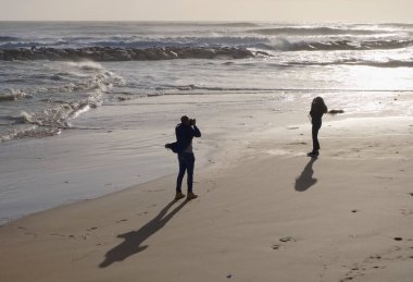 İtalya, Sicilya, Akdeniz, Marina di Ragusa (Ragusa Eyaleti), sahilde bir kadının fotoğraflarını çeken fotoğrafçı.