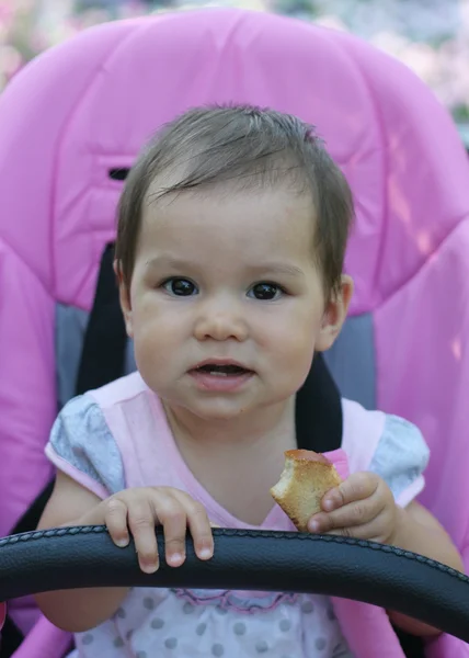 Girl seating in baby carriage and eating crouton — Stock Photo, Image