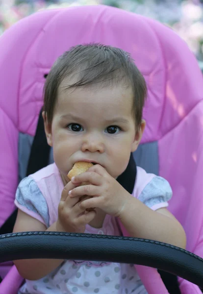Girl seating in baby carriage and eating crouton — Stock Photo, Image