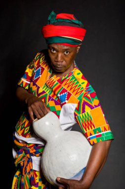 Geleneksel giyinmiş, dişlek gülüşlü, gri arka planda Afrikalı bir adam.