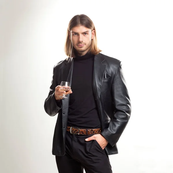 黒のスーツを着てブランデーのガラスと若い男ブロンドの髪の肖像画は 灰色の背景の上にポーズ クラシックスタイル スタジオショット — ストック写真
