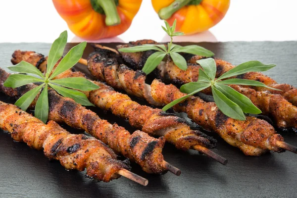 Etwas eingewickeltes Fleisch spießt auf einer Schiefertafel, die mit zwei Paprika dekoriert ist — Stockfoto