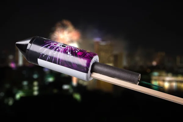 Unused pyrotechnics rocket in front of a blurry city with firewo — Stock Photo, Image