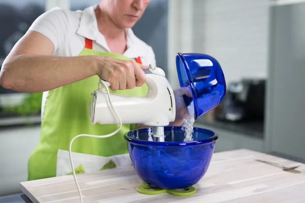 Een vrouw is het gieten van sommige poeder in een kom van het deeg en maakt gebruik van een roerder — Stockfoto