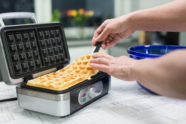 Woman is turning the waffles on a waffle iron in their kitchen — Stock Photo, Image