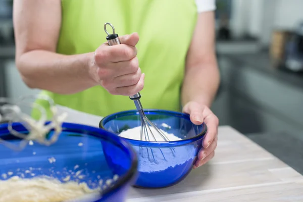 La mujer está removiendo la masa con un batidor de huevos en un tazón azulado en él — Foto de Stock