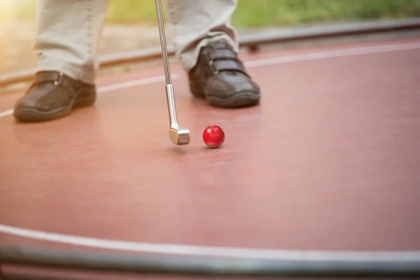 Homem está colocando uma bola de golfe vermelho com sua raquete de ferro — Fotografia de Stock