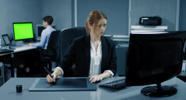 4K: Una mujer de negocios está trabajando en una tableta gráfica en su escritorio. Otra mujer de negocios está trabajando en el fondo con una pantalla de Greenkey . — Vídeos de Stock