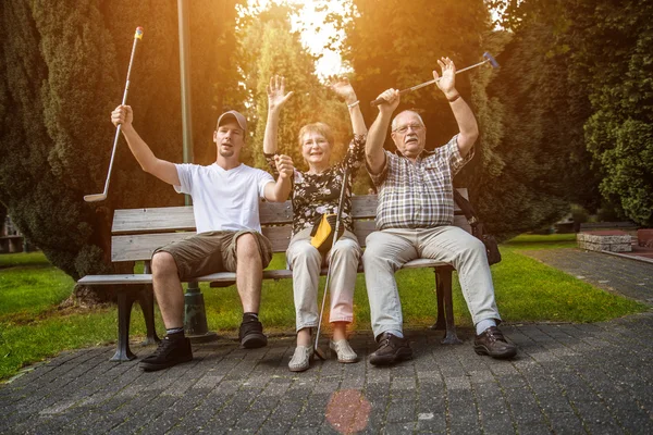 Två generation av en familj som sitter på en parkbänk vid en minigolfbana domstol — Stockfoto