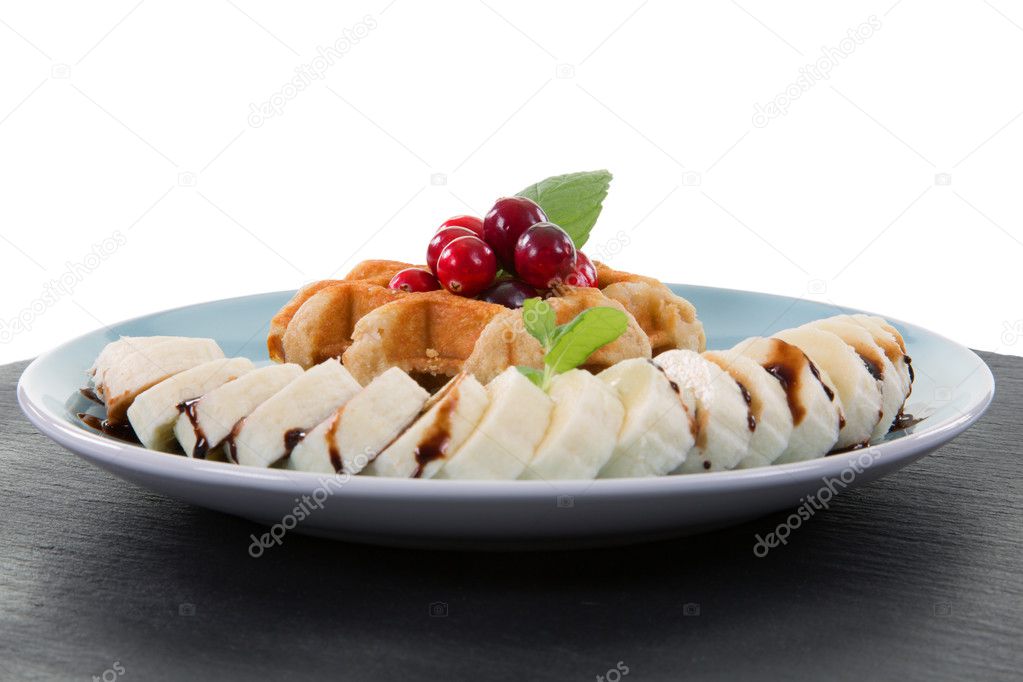 Waffle with cranberries and a sliced banana with chocolate on a blueish plate
