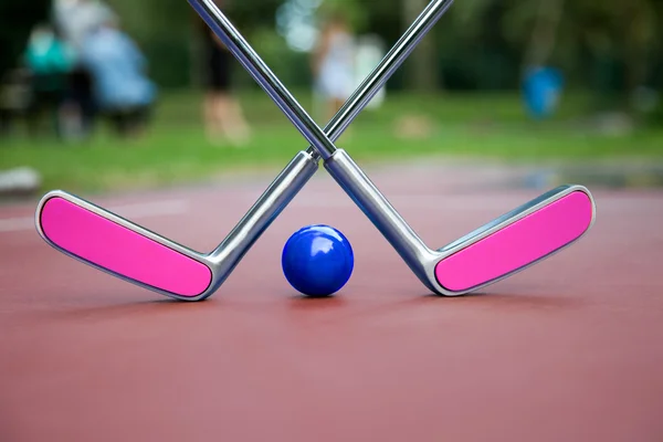 Dos raquetas de hierro cruzado rosado y una bola azulada construyendo un paisaje de minigolf Imagen de archivo